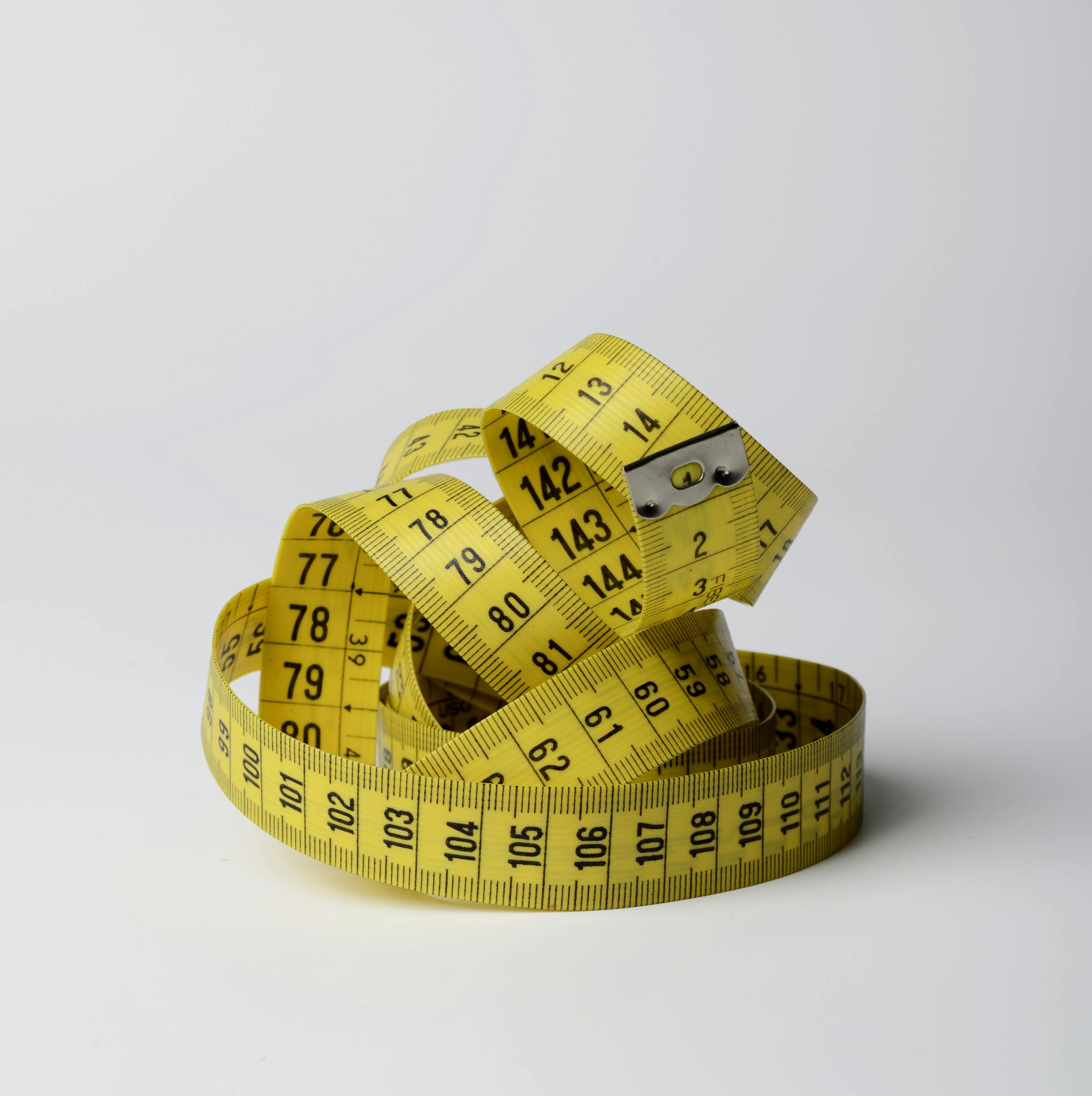 A bright yellow measuring tape coiled in loops, showcasing measurements clearly against a white background.
