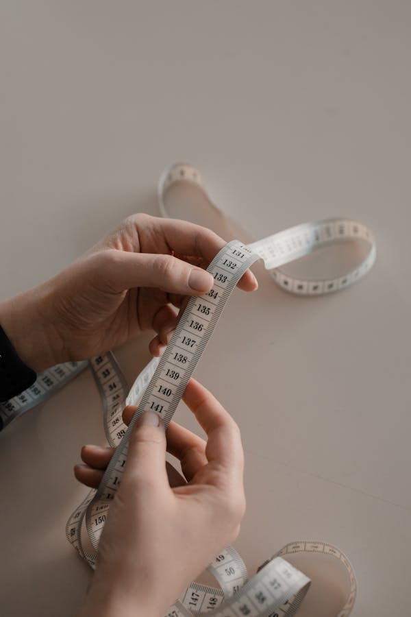 Photo by Ron Lach Close-up of hands holding a white measuring tape, ideal for sewing concepts.