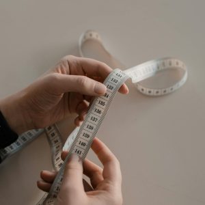 Photo by Ron Lach Close-up of hands holding a white measuring tape, ideal for sewing concepts.